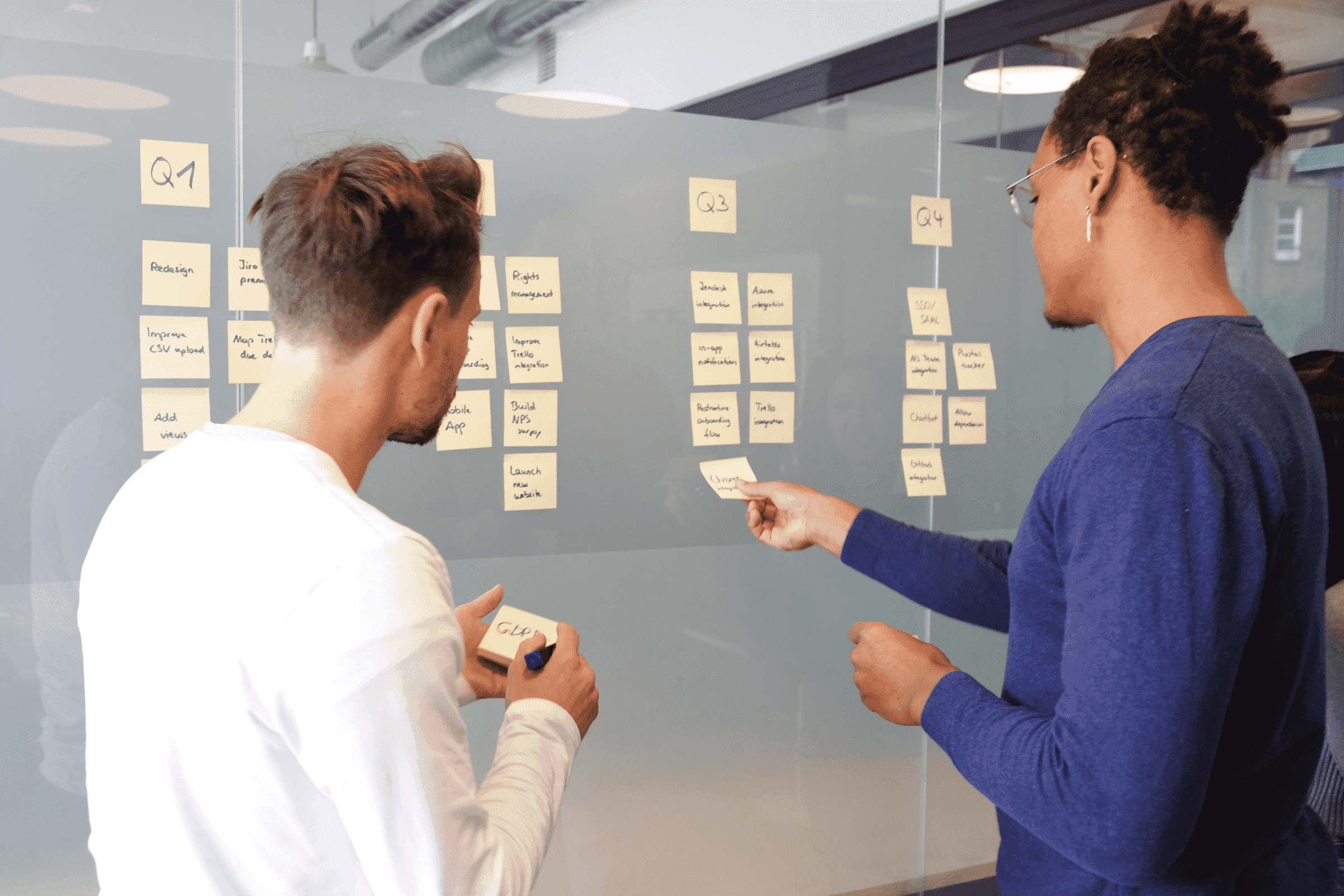 Two people put post-it notes on a wall while discussing ideas.